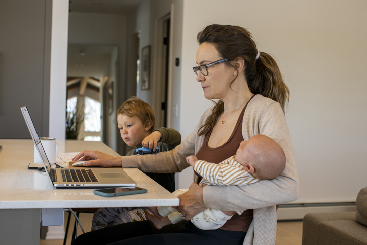 mother working on home computer, holding baby, sitting next to child