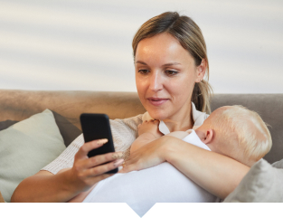 Baby sleeping in mother's arms while she looks at her phone