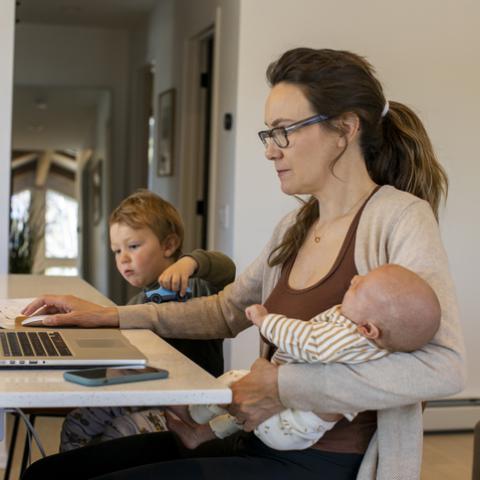 mother working on home computer, holding baby, sitting next to child